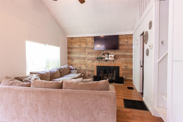 living room featuring visible vents, a large fireplace, wood walls, vaulted ceiling, and wood finished floors