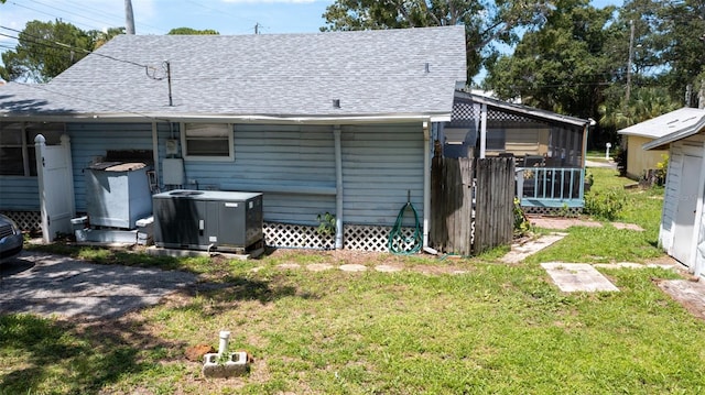 back of property featuring a yard, cooling unit, and a shingled roof