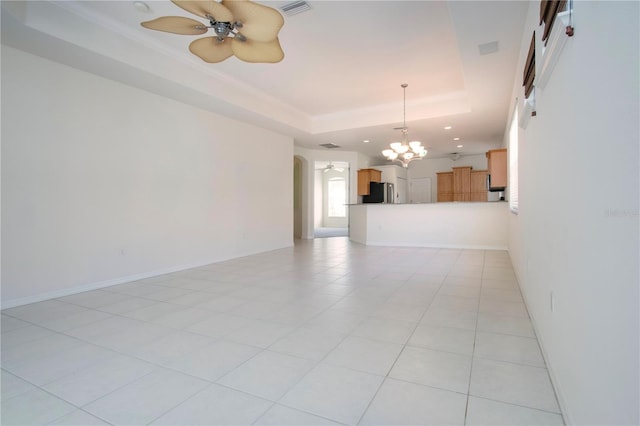 unfurnished living room with a raised ceiling, ceiling fan with notable chandelier, arched walkways, light tile patterned floors, and baseboards