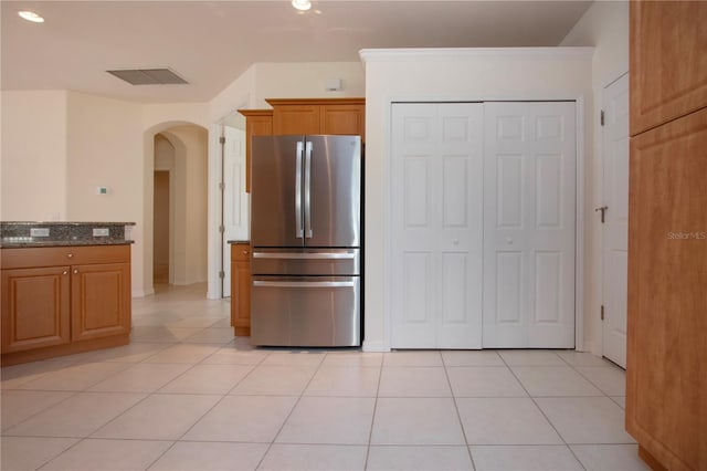 kitchen with visible vents, light tile patterned floors, dark stone countertops, freestanding refrigerator, and arched walkways