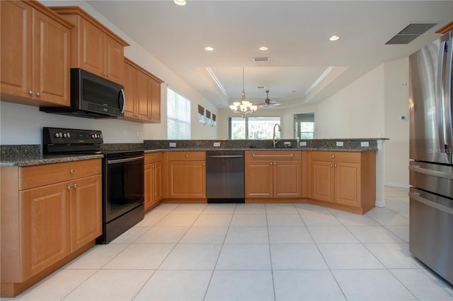 kitchen with dark stone counters, a peninsula, a sink, stainless steel appliances, and a raised ceiling