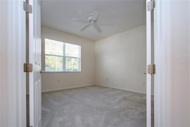 carpeted spare room with a ceiling fan and baseboards