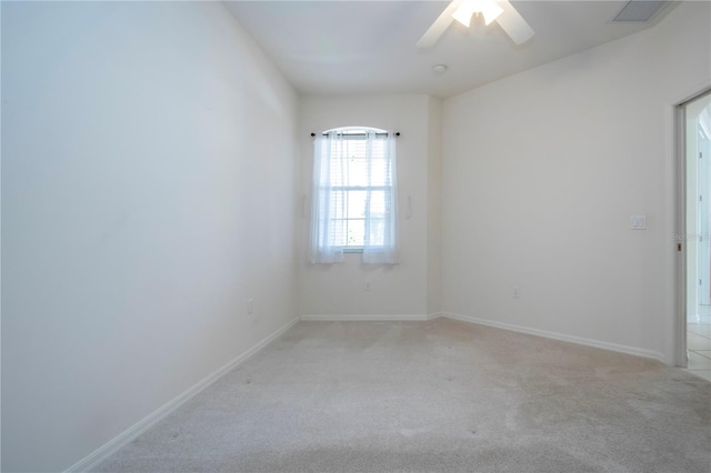 empty room featuring a ceiling fan, light colored carpet, visible vents, and baseboards