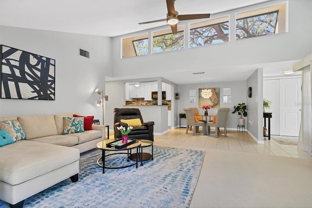 living room featuring light tile patterned floors, a ceiling fan, visible vents, baseboards, and a high ceiling