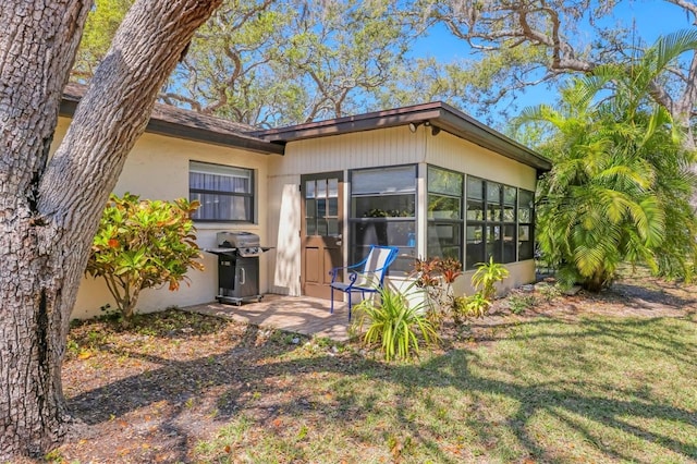 rear view of house featuring stucco siding, a sunroom, a yard, and a patio area