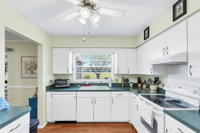 kitchen with white appliances, dark countertops, under cabinet range hood, and a sink