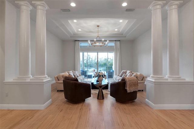 living area featuring a raised ceiling, ornate columns, and wood finished floors