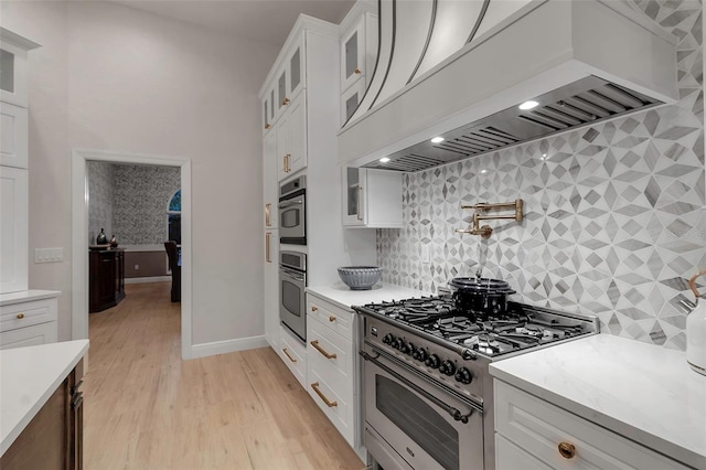 kitchen featuring glass insert cabinets, custom range hood, light wood-style flooring, white cabinets, and stainless steel appliances