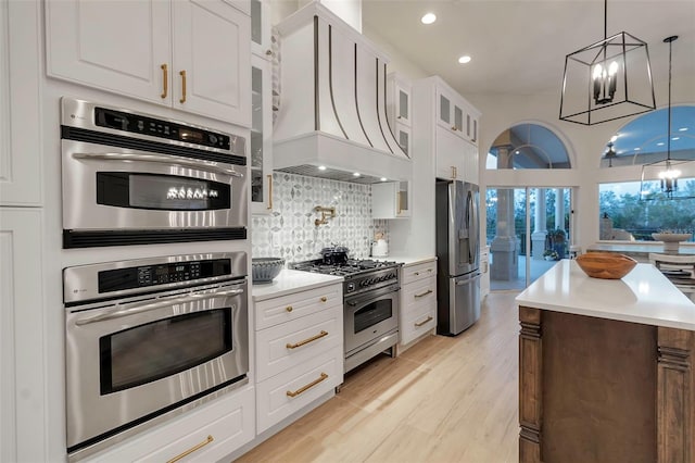 kitchen featuring light wood finished floors, custom range hood, glass insert cabinets, appliances with stainless steel finishes, and tasteful backsplash