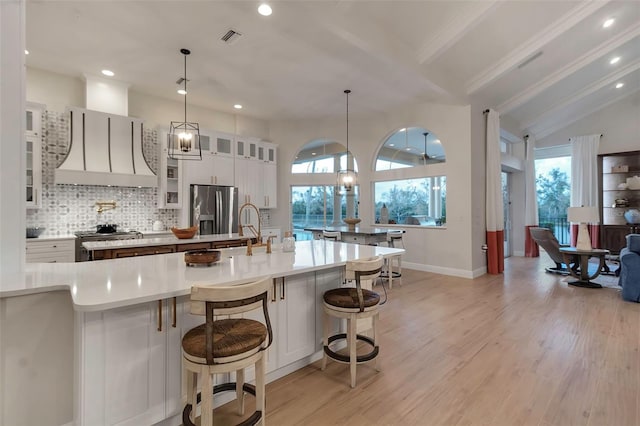 kitchen with visible vents, premium range hood, light wood-type flooring, stove, and stainless steel fridge