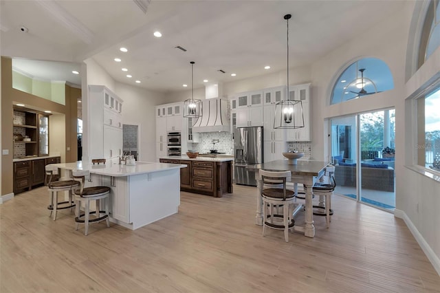 kitchen with premium range hood, a large island, appliances with stainless steel finishes, a kitchen bar, and light wood-type flooring