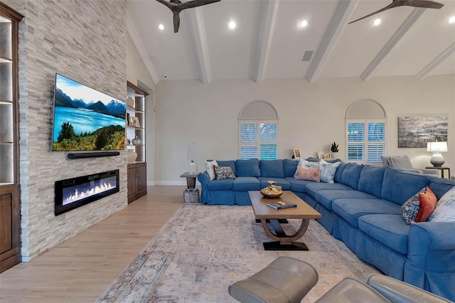 living area with beamed ceiling, built in features, a stone fireplace, light wood finished floors, and ceiling fan