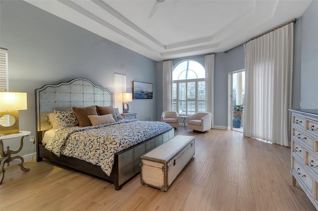 bedroom featuring access to exterior, baseboards, light wood-style floors, and a tray ceiling