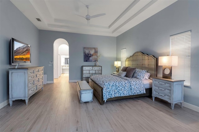 bedroom featuring a raised ceiling, arched walkways, visible vents, and light wood-type flooring