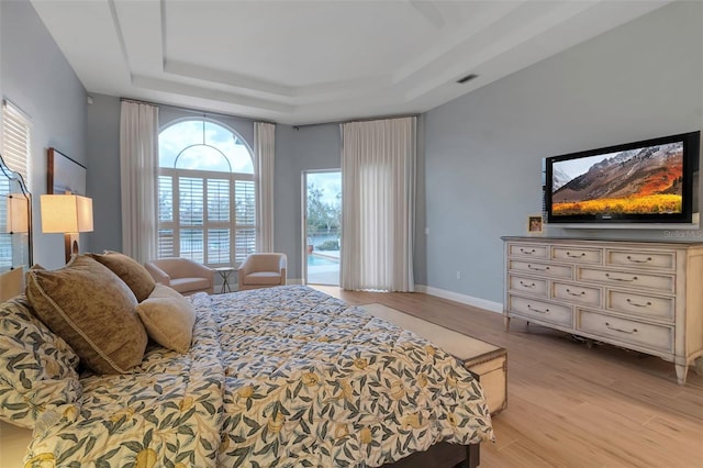 bedroom with visible vents, access to outside, a tray ceiling, light wood finished floors, and baseboards