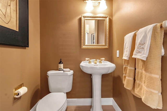 half bath featuring baseboards and toilet