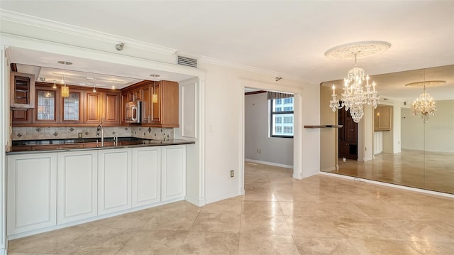 kitchen with dark countertops, brown cabinets, stainless steel microwave, a notable chandelier, and tasteful backsplash