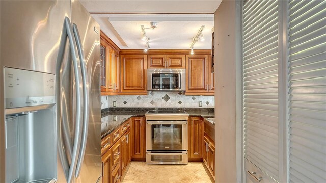 kitchen featuring dark stone countertops, light tile patterned floors, stainless steel appliances, decorative backsplash, and brown cabinets