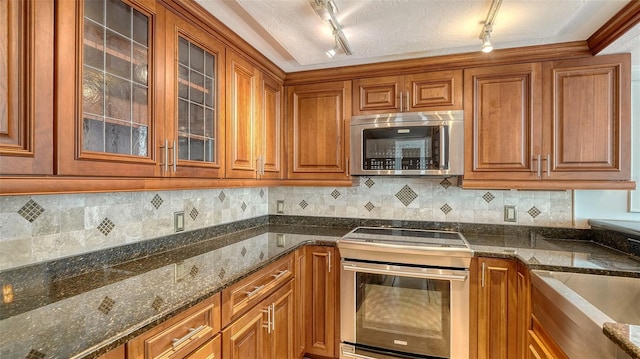 kitchen featuring dark stone countertops, stainless steel appliances, brown cabinets, and backsplash