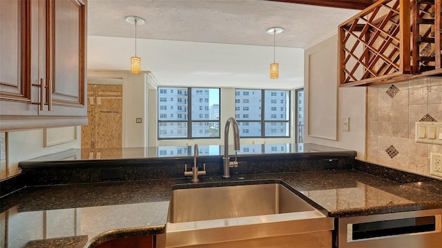 kitchen with a sink, dark stone counters, tasteful backsplash, and pendant lighting