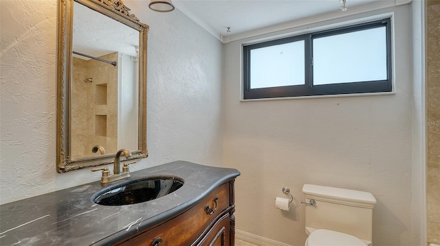 bathroom featuring vanity, toilet, a textured wall, and ornamental molding