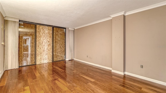 empty room with crown molding, wood finished floors, baseboards, and a textured ceiling