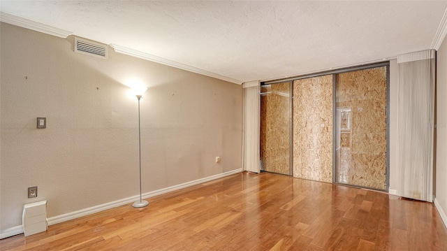 empty room with crown molding, wood finished floors, visible vents, and a textured ceiling