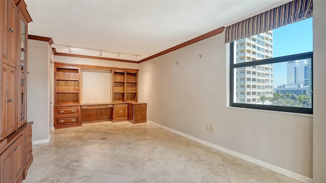 unfurnished office featuring a city view, track lighting, built in features, crown molding, and baseboards