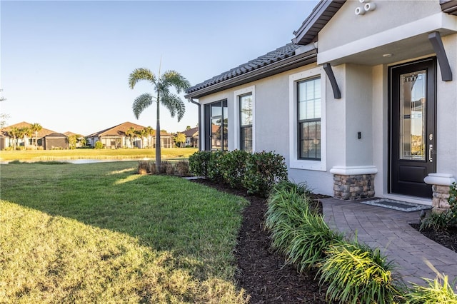 exterior space with stucco siding, stone siding, a lawn, and a tile roof