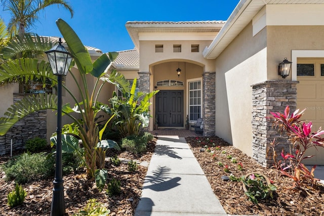 view of exterior entry with stucco siding, stone siding, an attached garage, and a tiled roof