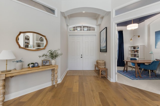 entrance foyer with arched walkways, baseboards, and wood finished floors