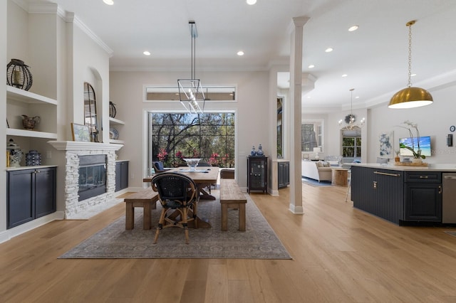 dining space with built in shelves, recessed lighting, ornamental molding, a stone fireplace, and light wood-type flooring