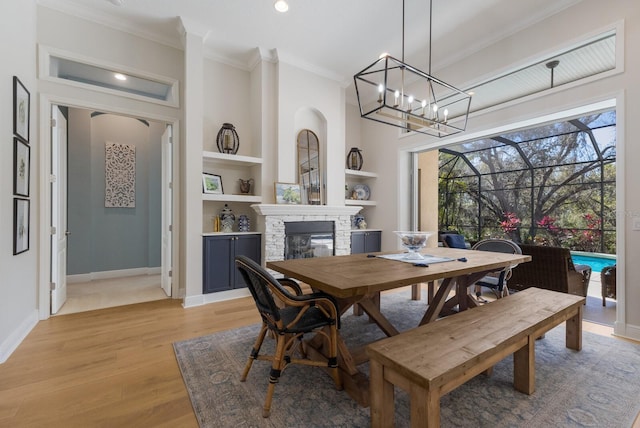 dining room with light wood-style flooring, built in features, a fireplace, crown molding, and baseboards