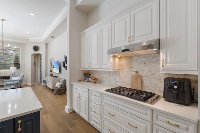 kitchen with light wood finished floors, under cabinet range hood, stainless steel gas cooktop, arched walkways, and white cabinetry