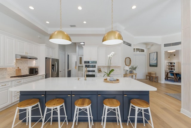 kitchen featuring under cabinet range hood, stainless steel appliances, a breakfast bar area, and white cabinets