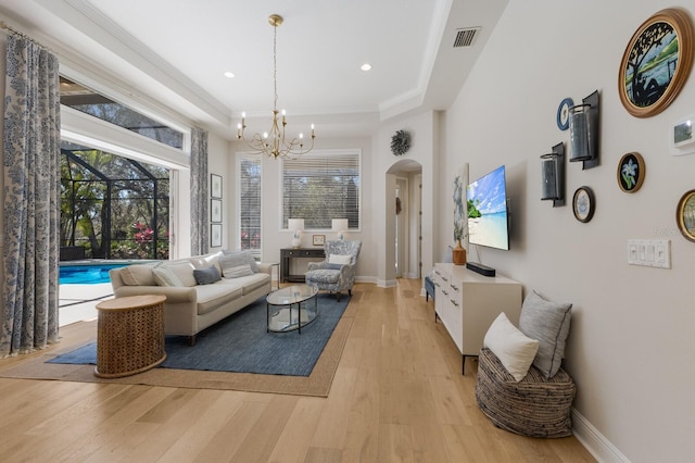 living room with visible vents, arched walkways, light wood-style floors, baseboards, and a chandelier