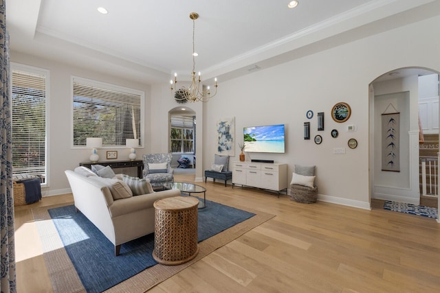 living area featuring arched walkways, light wood finished floors, a raised ceiling, and baseboards