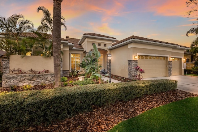 mediterranean / spanish-style home featuring stucco siding, stone siding, concrete driveway, an attached garage, and a tiled roof