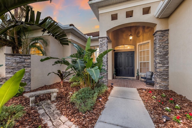 exterior entry at dusk featuring stone siding and stucco siding