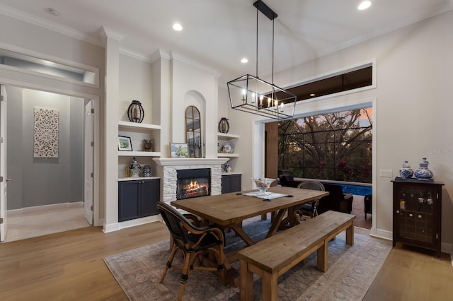 dining area with a stone fireplace, light wood-style flooring, ornamental molding, and an inviting chandelier