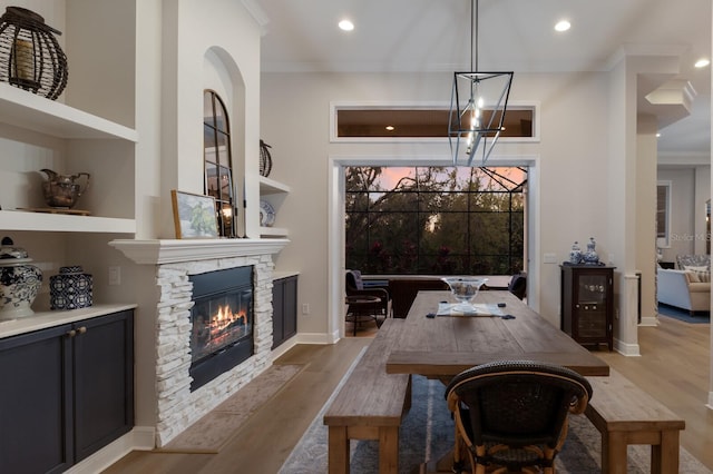 dining room featuring light wood-type flooring, a notable chandelier, ornamental molding, recessed lighting, and a stone fireplace