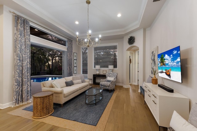 living area featuring ornamental molding, wood finished floors, arched walkways, an inviting chandelier, and baseboards