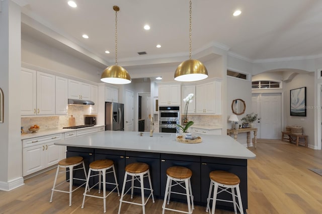 kitchen with under cabinet range hood, stainless steel appliances, a breakfast bar, and white cabinetry