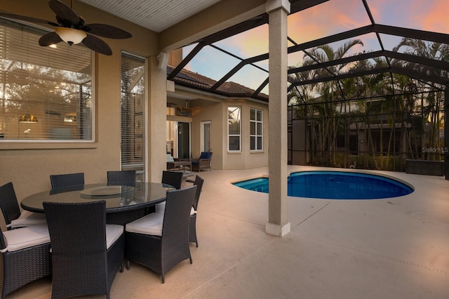 pool at dusk featuring outdoor dining space, a ceiling fan, a patio, an outdoor pool, and a lanai