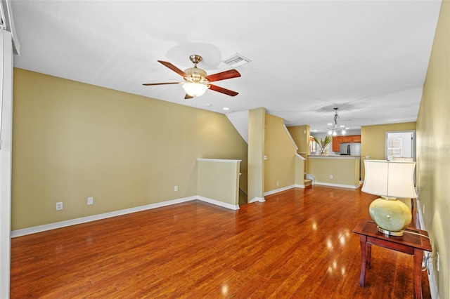 unfurnished living room featuring visible vents, baseboards, wood finished floors, and ceiling fan with notable chandelier