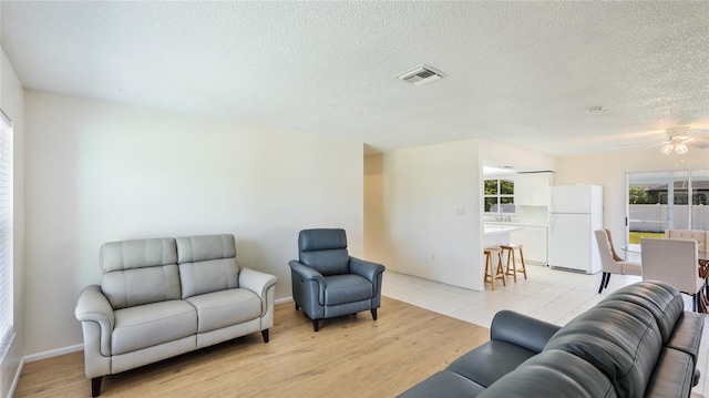 living area featuring visible vents, light wood-style flooring, a textured ceiling, and ceiling fan