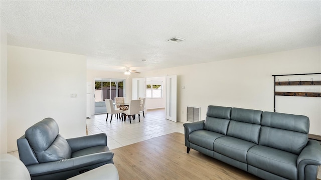 living room with light tile patterned flooring, visible vents, a textured ceiling, and ceiling fan