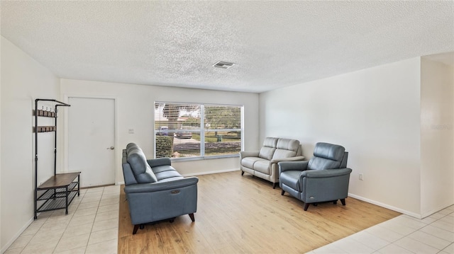 living room with baseboards, light wood-style floors, visible vents, and a textured ceiling