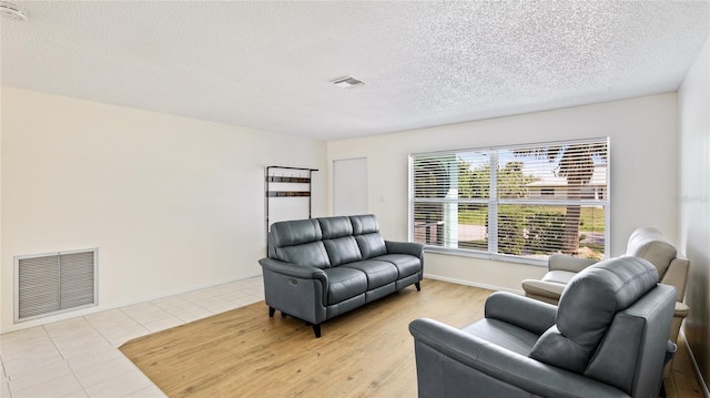 living area featuring light tile patterned floors, baseboards, visible vents, and a textured ceiling