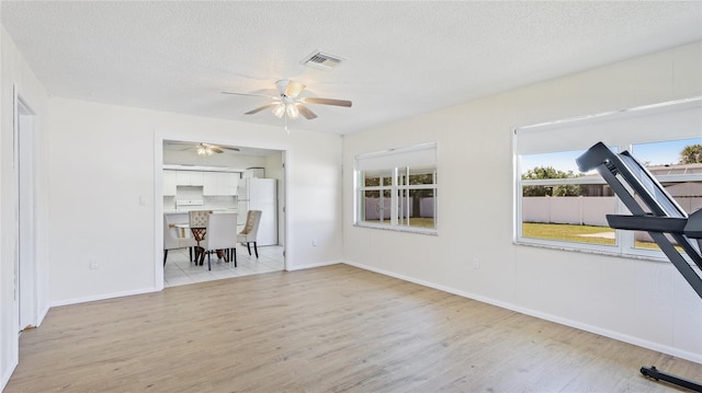 unfurnished living room featuring a textured ceiling, visible vents, light wood finished floors, and ceiling fan